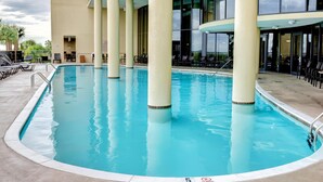 A swimming pool with lounge chairs and tables, surrounded by a building with large windows and columns. - Two-bedroom Apartment (Dauphin Island)
