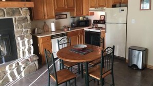 Une cuisine avec des meubles de rangement en bois, une cheminée en pierre, une table à manger avec des chaises et un réfrigérateur.