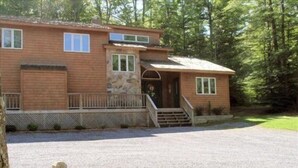 A two-story wooden house with a stone accent wall, a front porch, and a gravel driveway. - Serenity (Davis)
