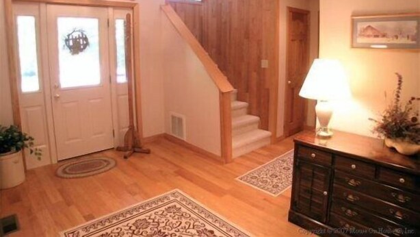 A wooden staircase leading to a second floor, a white door with a window, and a dark wooden dresser with a lamp. - Serenity (Davis)