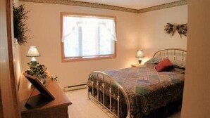 A bedroom with a bed, a nightstand, a lamp, a window with blinds, and a wall-mounted decoration. - Serenity (Davis)