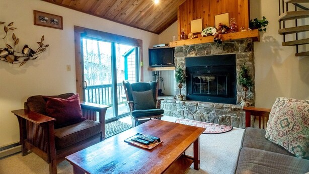 Un salon chaleureux avec une cheminée en pierre, un plafond en bois et un coin salon confortable.