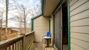 Une terrasse en bois avec une chaise bleue et une petite table, donnant sur un quartier résidentiel bordé d’arbres et de maisons.