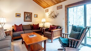 Un salon chaleureux avec un plafond en bois, un ensemble de canapés, une table basse et un fauteuil offrant une vue sur l’extérieur.