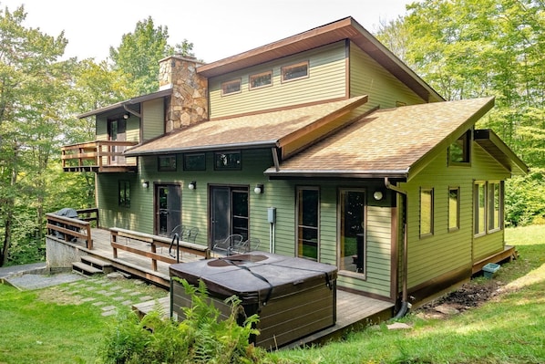 A two-story house with a deck, a hot tub, and a stone chimney.