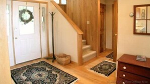 A wooden staircase leading to a second floor, a door with a wreath, and a wooden cabinet with a mirror.