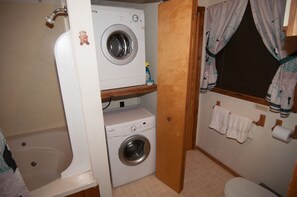 Un lavadero pequeño con lavadora, secadora y una ventana con cortinas.