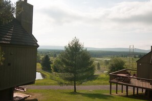 A view from a porch overlooking a grassy area with a tree, a body of water, and distant hills. - Mountain Magic (Davis)