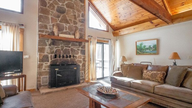 A cozy living room with a stone fireplace, a television, a sofa, and a table with a bowl of snacks. - Mountain Treat (Davis)