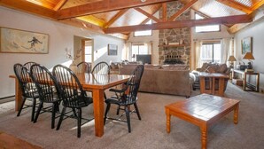 A spacious living area with a high wooden ceiling, a stone fireplace, and a dining area with a wooden table and chairs. - Mountain Treat (Davis)