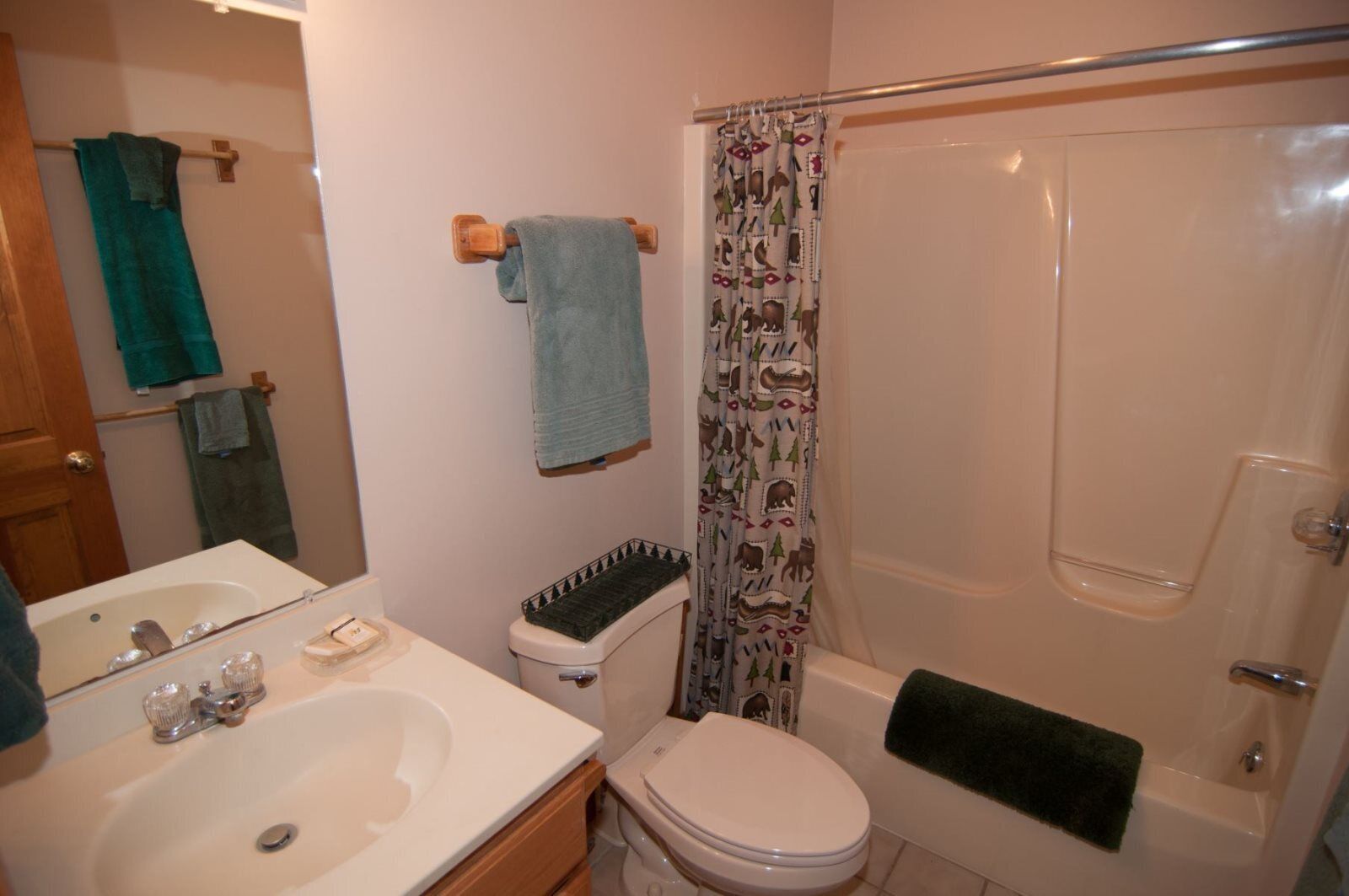 Une salle de bain avec un lavabo, des toilettes et une baignoire. Des serviettes sont accrochées au mur et il y a un rideau de douche à motifs.