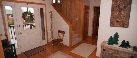A wooden staircase leading to a second floor, a door with a glass panel, a chair, and a small table with a basket.