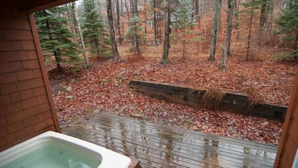 Una terraza de madera con un jacuzzi, rodeada por un bosque de hojas otoñales.