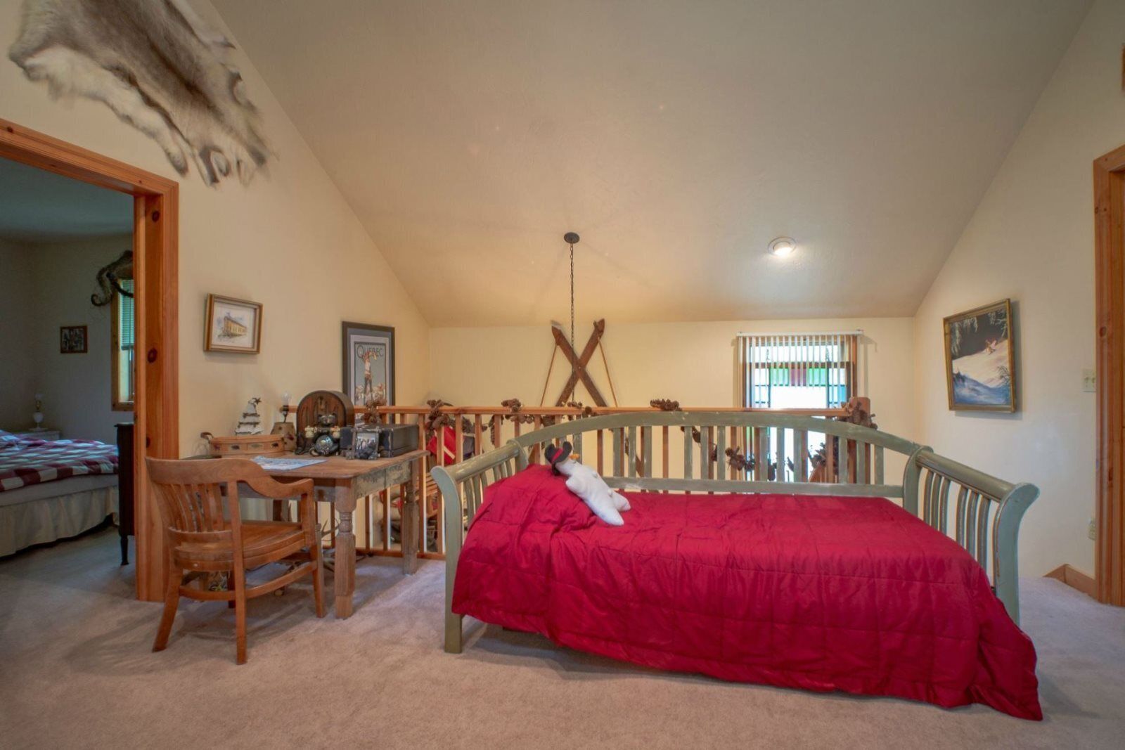 A bedroom with a bed, a desk, and a chair. There is a window with blinds and a painting on the wall.