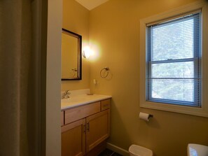 A bathroom with a white sink, wooden cabinets, a mirror, a toilet, and a window with blinds.