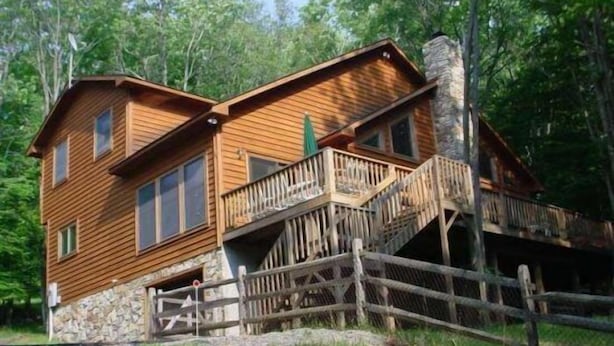 A two-story log cabin with a stone foundation, a wooden deck, and a staircase leading to the upper level. - Laird`s Retreat (Davis)
