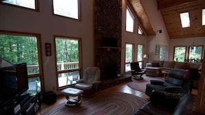 A spacious living room with a stone fireplace, large windows, and a high ceiling. - Laird`s Retreat (Davis)