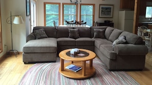 A cozy living room with a sectional sofa, a round coffee table, and a view of the kitchen through large windows. - Laird`s Retreat (Davis)