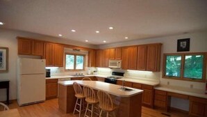A modern kitchen with wooden cabinets, a central island with bar stools, and a built-in microwave. - Laird`s Retreat (Davis)