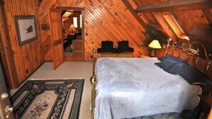 A bedroom with a wooden ceiling, a bed, a nightstand, a lamp, and a rug. - Mingo Lodge (Davis)