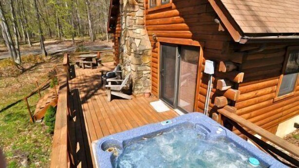 A wooden cabin with a stone chimney, a hot tub, and a deck with outdoor seating. - Mingo Lodge (Davis)