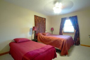 Quarto com duas camas, ventilador de teto e janela com cortinas.