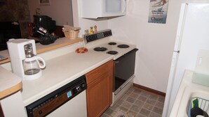 A compact kitchen with a white stove, a microwave, and a coffee maker. There is a wooden cabinet and a tiled backsplash. - Herzwoods D304 (Davis)