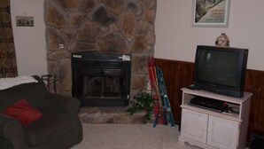 A living room with a stone fireplace, a television on a stand, and skis leaning against the wall. - Herzwoods D304 (Davis)