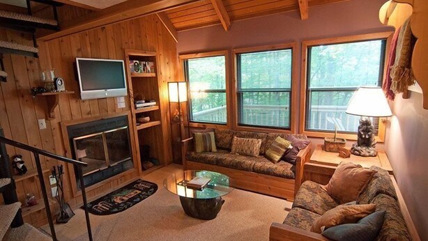 L’intérieur d’un chalet accueillant, avec une cheminée, des murs en bois, un canapé et un téléviseur.