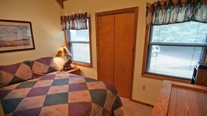 Une chambre à coucher comprenant un lit, une table de chevet, une lampe, une table en bois, une armoire et une fenêtre avec des rideaux.