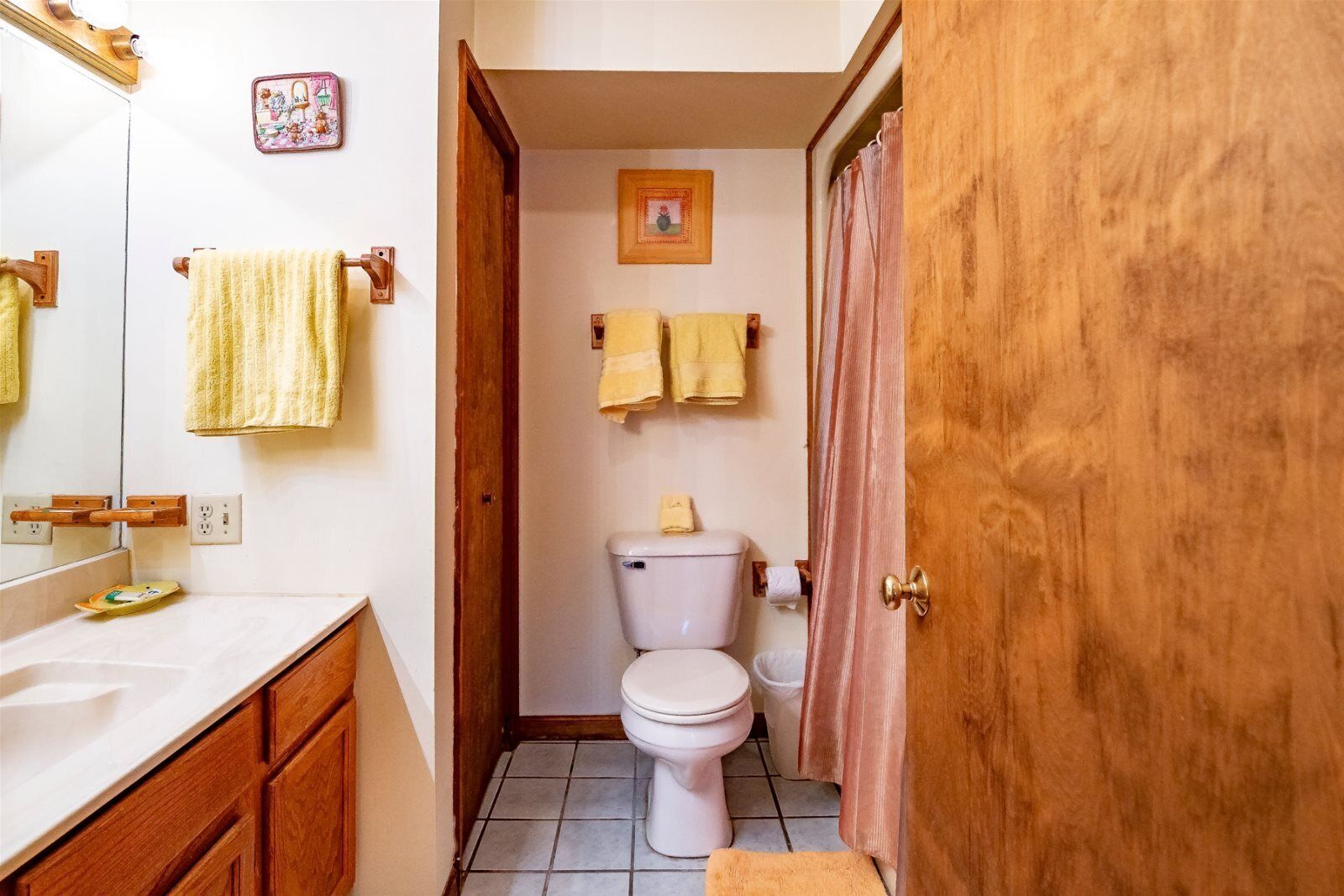 A bathroom with a white toilet, wooden cabinets, a mirror, and two towels hanging on the wall.