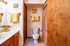 A bathroom with a white toilet, wooden cabinets, a mirror, and two towels hanging on the wall. - Herzwoods C103 (Davis)