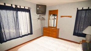 Quarto com cama, cômoda, televisão e cortinas.