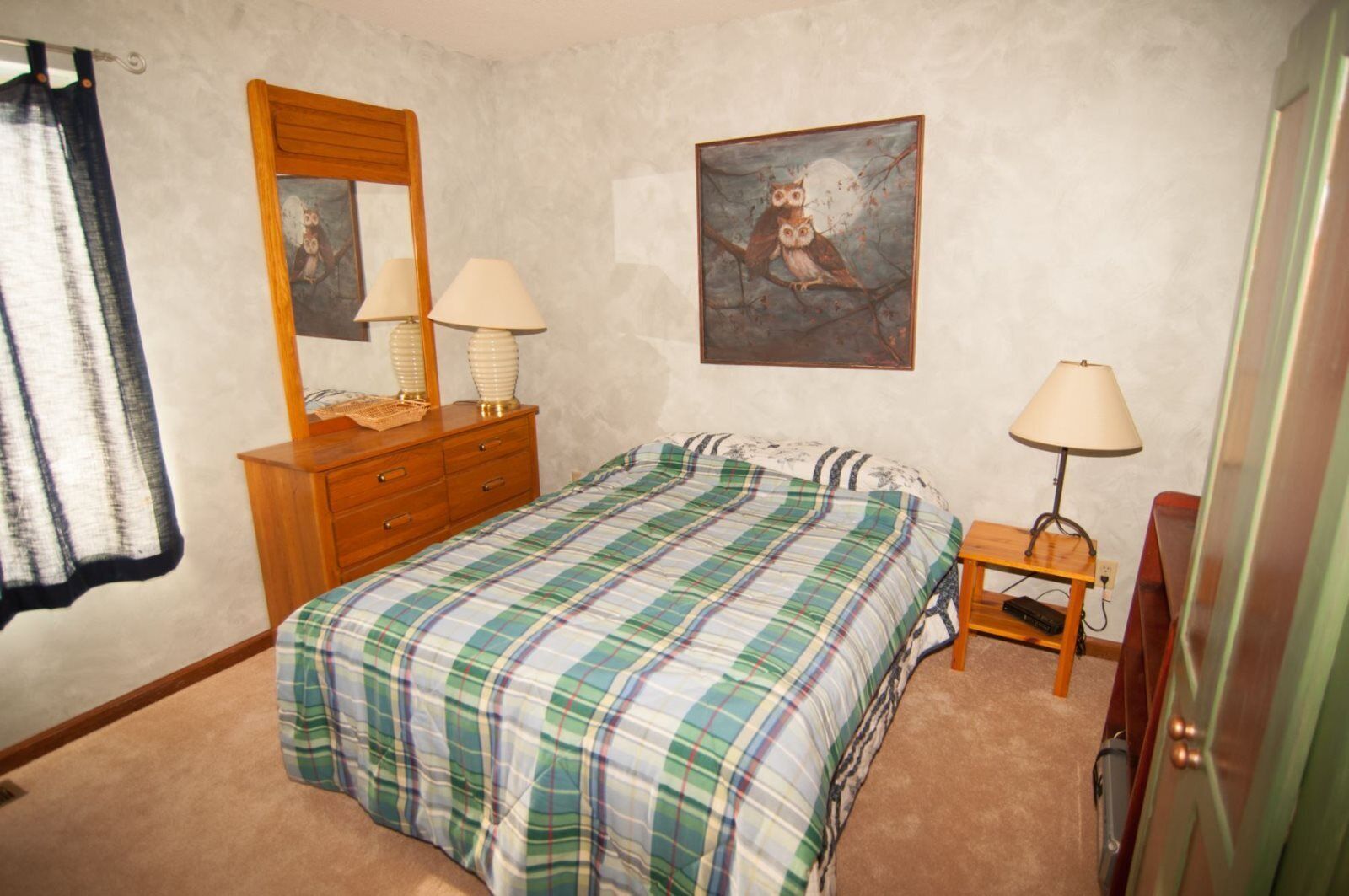 A bedroom with a bed, two bedside lamps, a dresser, a mirror, and a painting on the wall.
