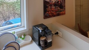 Una cocina con cafetera, una ventana con persianas y tres cuadros en la pared.