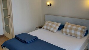Un dormitorio con cama, ventilador de techo, unidad de aire acondicionado y mesita de noche con lámpara.