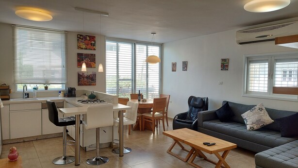 Un apartamento moderno con cocina, comedor y sala de estar. Cuenta con un ventanal grande, un sofá y una mesa de centro.