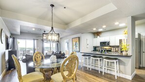 A spacious kitchen with a central island, white cabinetry, and a dining area with a glass table and ornate chairs. - Pool Access + Private Deck: Lake Ozark Retreat (Lake Ozark)