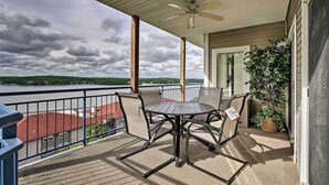A covered outdoor balcony with a table and chairs, a ceiling fan, and a view of a body of water and buildings. - Pool Access + Private Deck: Lake Ozark Retreat (Lake Ozark)