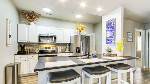 A modern kitchen with white cabinets, stainless steel appliances, and a central island with bar stools. - Pool Access + Private Deck: Lake Ozark Retreat (Lake Ozark)