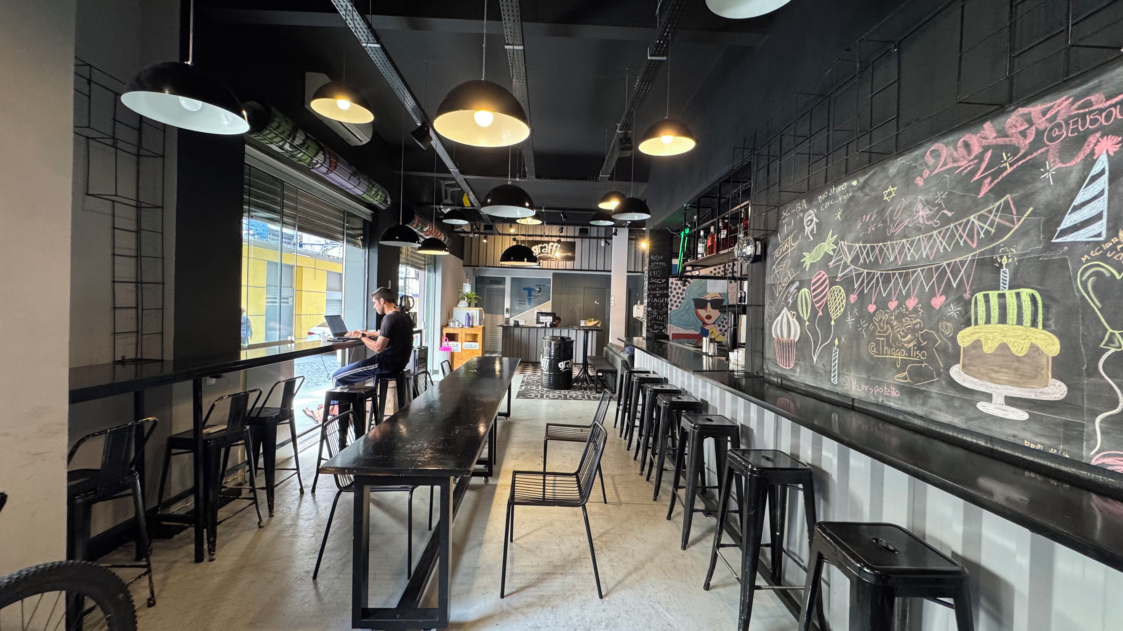 An interior with a long counter, multiple stools, and a chalkboard with drawings.