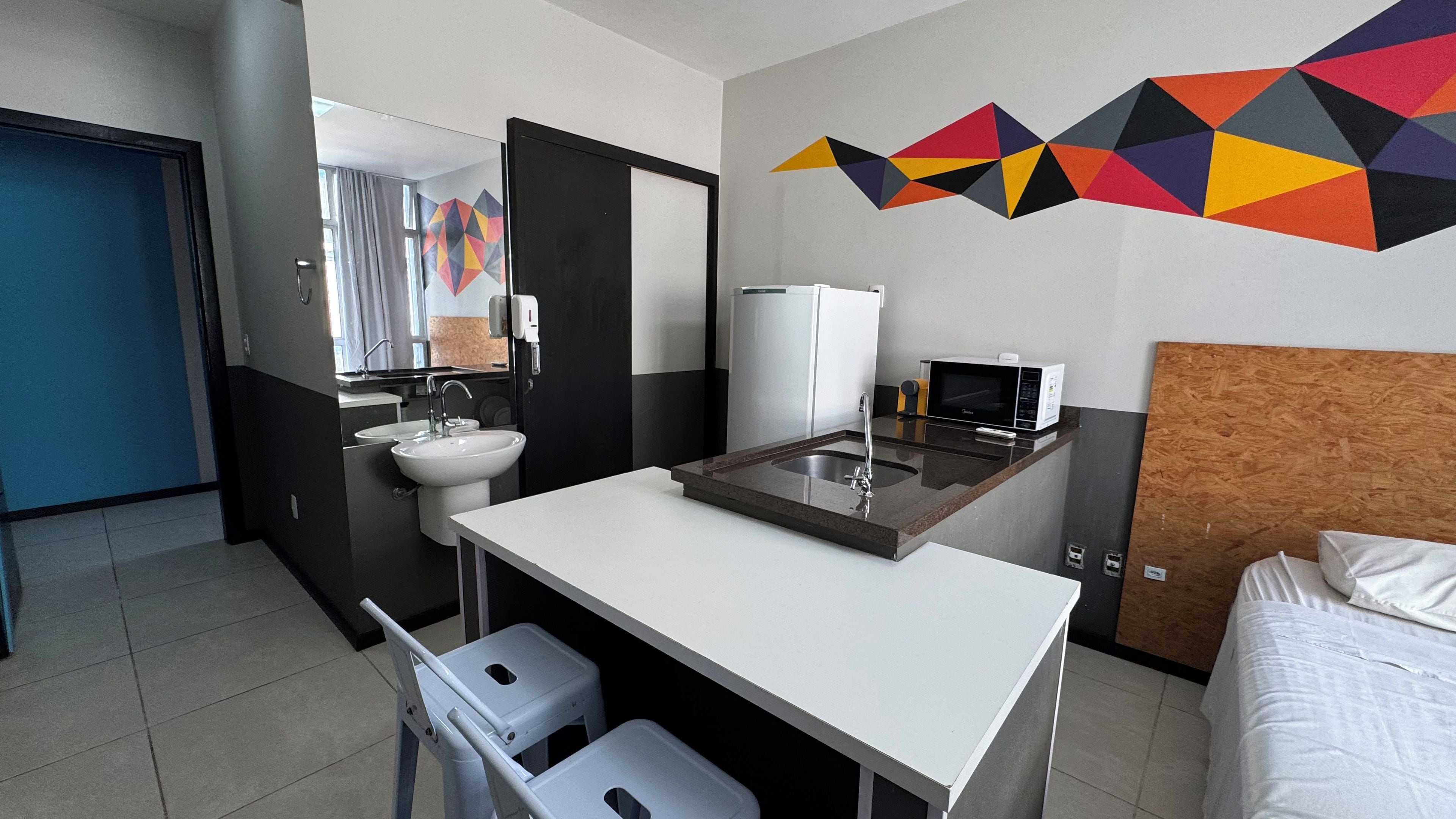 Habitación de hotel con cama, escritorio con lavamanos, microondas y espejo.
