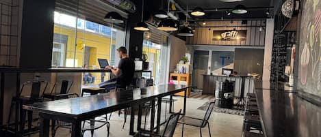 Zona de bar interior con mesas y sillas, un mostrador de recepción y un menú en una pizarra.