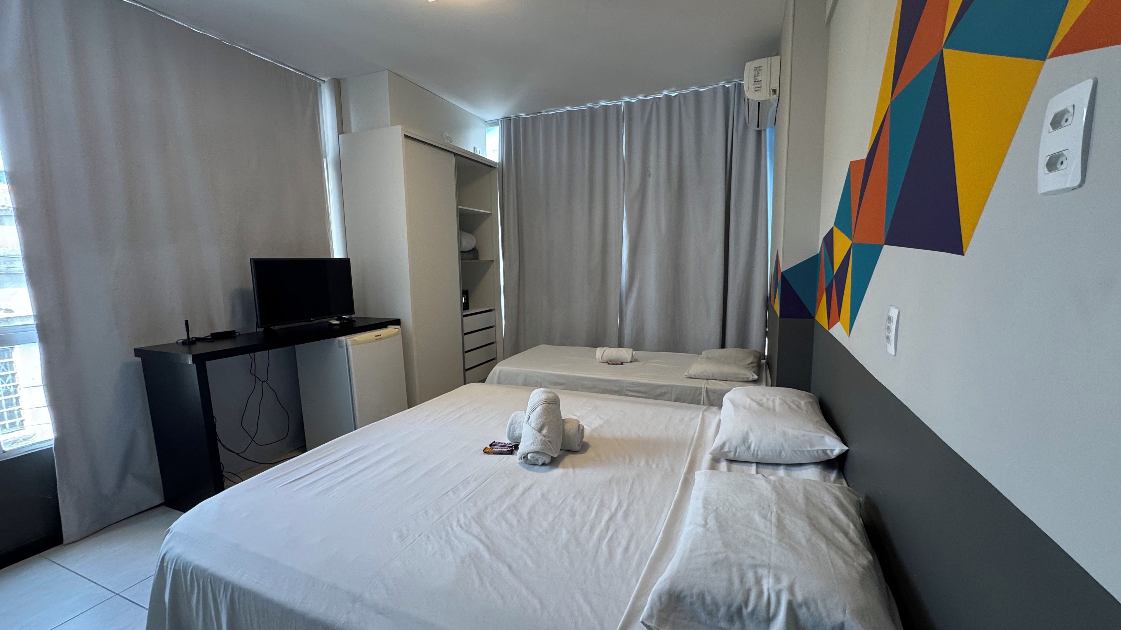 A hotel room with two beds, a desk with a television, and a wardrobe.