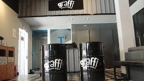 Twee vaten met 'graffi' branding in een ontvangsthal met een geruit vloertje en een bordje erboven dat 'KAMERS 1-12' aangeeft.