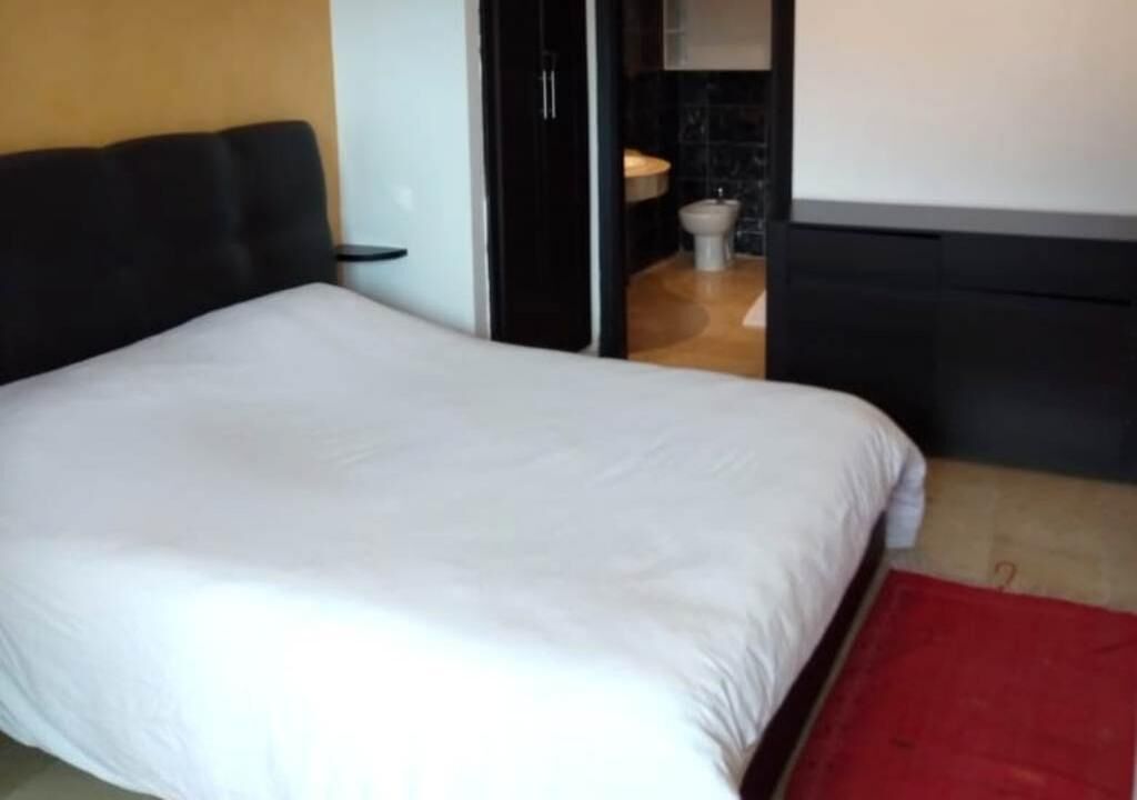 A bedroom with a bed, a red rug, and a bathroom visible through an open door.