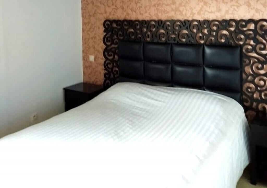 A neatly made bed with a dark headboard and a plain wall in the background.