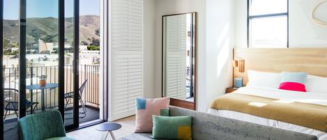 A modern hotel room with a balcony, a bed with multiple pillows, a sofa, and a large mirror.