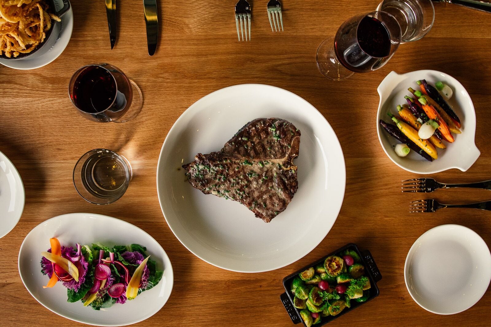 A dining table with various dishes, including a steak, vegetables, and a salad.