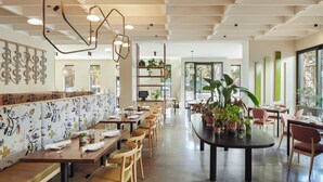 A modern restaurant with wooden tables and chairs, a long counter with seating, and decorative plants. - Hotel San Luis Obispo (San Luis Obispo)